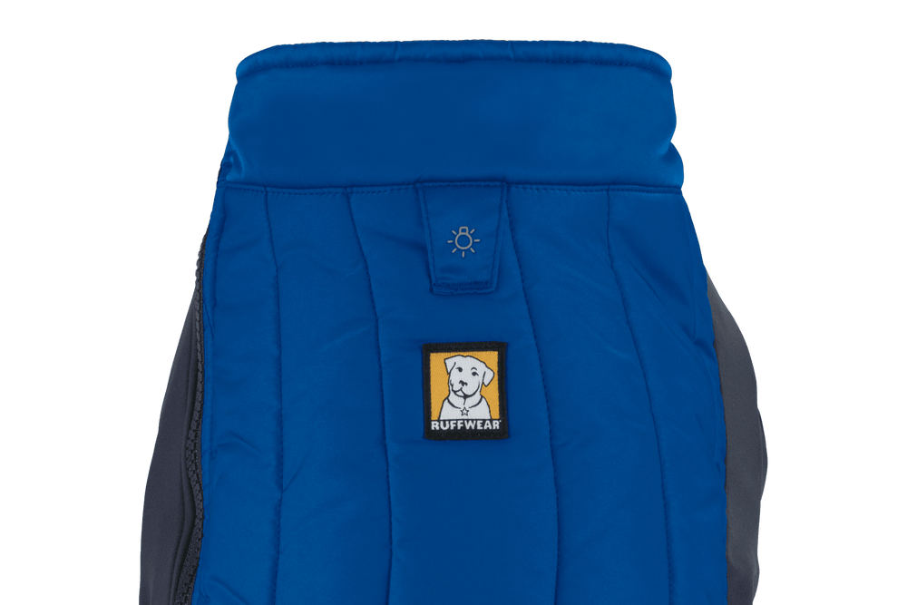 Blauer Hundemantel von Ruffwear mit gestepptem Design und hohem Kragen, gelbes Hundekopf-Logo in der Mitte.