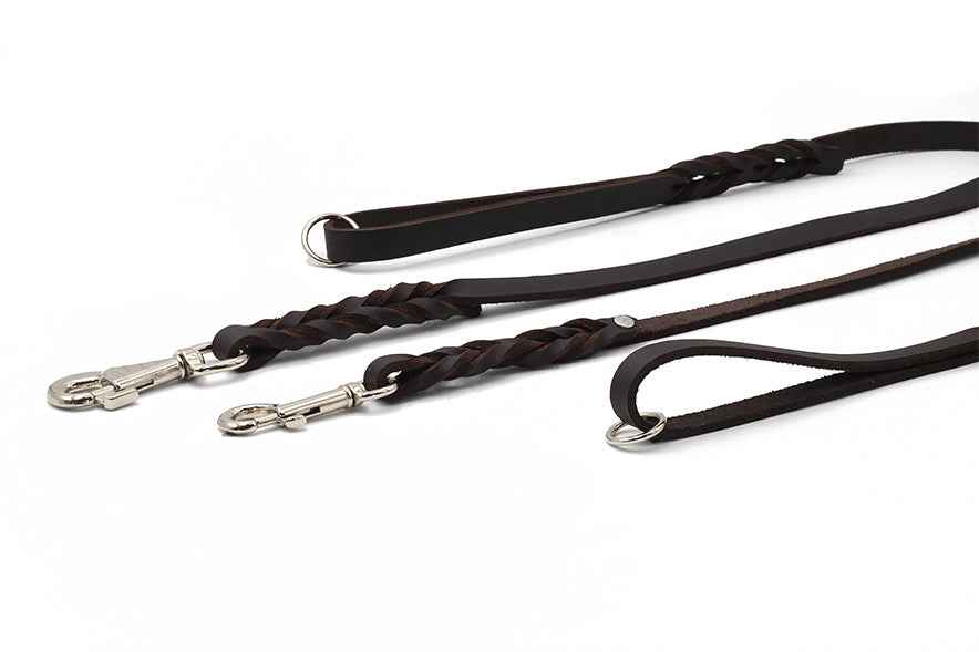 Zwei dunkelbraune Fettleder-Hundeleinen: eine geflochten, eine schlicht, beide mit metallenen Karabinerhaken und Schlaufen.