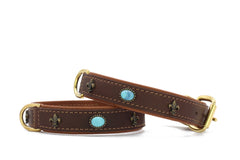 "Zwei elegante braune Lederhundehalsbänder mit goldfarbenen Beschlägen und blauen Steinelementen, verziert mit Lilienmotiv."