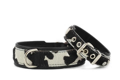 Zwei Halsbänder aus Kunstfell im Kuhmuster, eines breit mit D-Ring, das andere schmal mit Druckknöpfen.