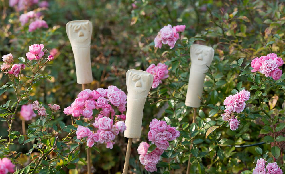 Stilisierte Figuren im Blumenbeet mit rosa Rosen, Teil des 3er-Sets Ohrwurmhaus für biologischen Pflanzenschutz.