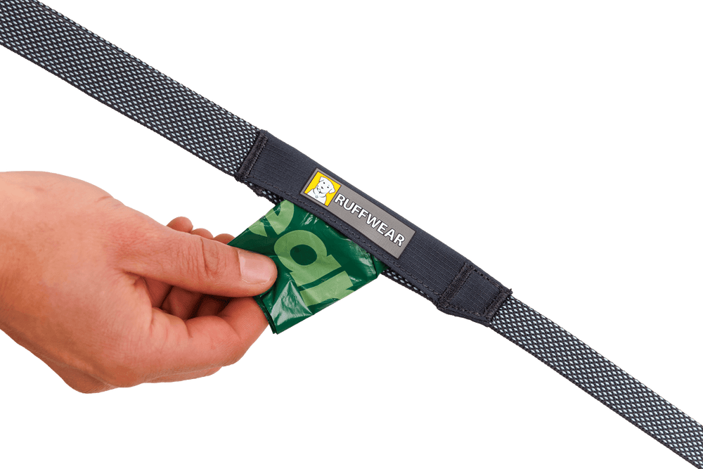 Hand nimmt grünes Paket aus Ruffwear Gürtel mit Netzstruktur und Logo-Aufnäher, ideal für die Hi Light™ Hundeleine.