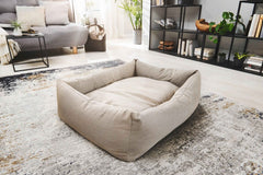 Beiges quadratisches CLASSIC Hundebett SMOOTH auf einem Teppich, umgeben von grauem Sofa und modernen Möbeln.