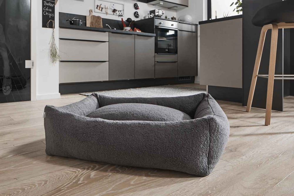 "Graues CLASSIC Hundebett TEDDY in moderner Küche, rechteckig mit erhöhtem Rand und rundem Kissen."