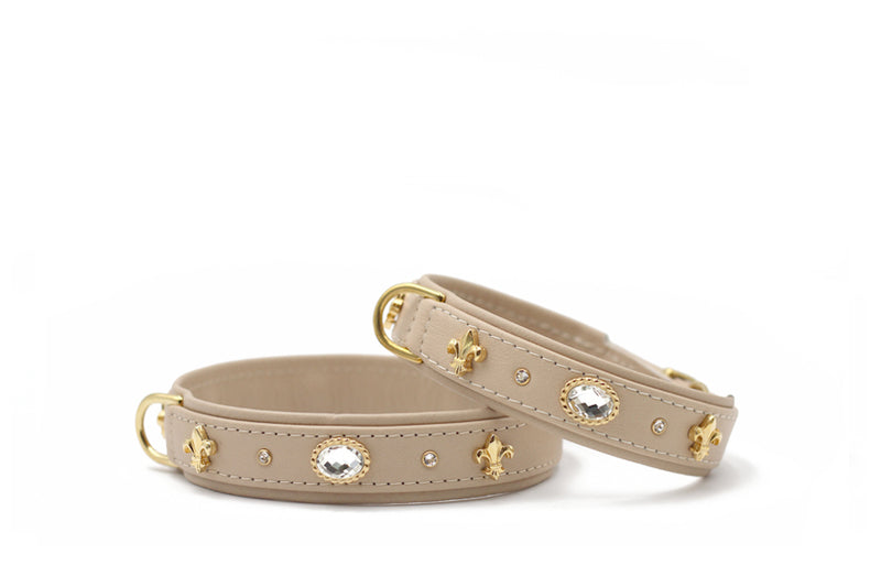 Zwei elegante beiger Lederarmbänder mit goldenen Fleur-de-Lis-Verzierungen und glitzernden Steinen.