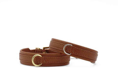 "Zwei schmale, elegante Armbänder aus braunem Leder mit goldener Schnalle und dekorativem Metallring."