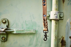 Braune Lederriemen-Leine mit Verzierung und schwarzem Karabinerhaken auf rostiger Metalloberfläche.