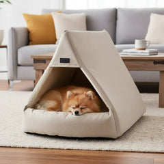 Kleiner Hund schläft friedlich in einem beige-farbenen Hundebett, im Hintergrund ein graues Sofa und dekorative Kissen.