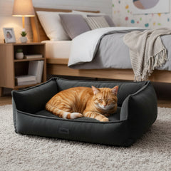 "Gemütliches, dunkles Katzenbett 'NILA' mit entspannter orangefarbener Katze im Schlafzimmer."