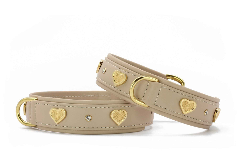 Beige Kunstlederarmbänder mit goldenen Herzmotiven und glitzernden Steinen, runde goldfarbene Verschlüsse.