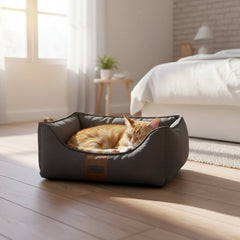 Entspannte orangefarbene Katze im grauen Komfortbett "ZALO" auf Holzfußboden in hellem Raum mit Fenster.