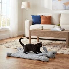 Grauer Hase-Teppich in hellem Raum mit schwarzem Kater und beigem Sofa mit bunten Kissen.