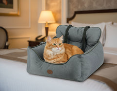 Gemütliches graues Katzenbett KADEK mit erhöhter Rückenlehne und Tragegurten, umgeben von einem stilvollen Hotelzimmer.