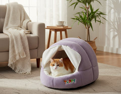 Gemütliche, lila Katzenhöhle mit orange-weißer Katze im hellen Wohnzimmer mit Sofa und Kaffeetisch.