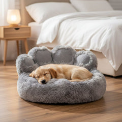 Schlafender Welpe in grauem, runden Hundebett in Pfotenform mit weichen Rändern auf einem gemütlichen Hintergrund.