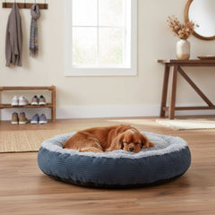 "Schlafender Hund auf rundem Komfortbett Donut Seda in gemütlicher, holzverkleideter Umgebung."