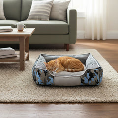 Katzenbett Elio mit einer entspannten orangefarbenen Katze in modernem Wohnraum, teppichbedeckt und mit Sofa im Hintergrund.