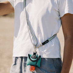 Person in T-Shirt und Shorts mit grüner Tasche am Hals vor sonnigem Strandhintergrund.