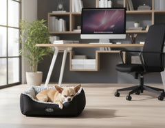 Kleiner Hund schläft friedlich in schwarzem Hundebett ARUSHA mit grauer Innenauskleidung, modernem Arbeitsplatz im Hintergrund.