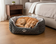 Schlafender Hund im ovalen Komfortbett SEOLI aus grauem Plüsch mit hellem Innenrand und Pfotenapplikation.