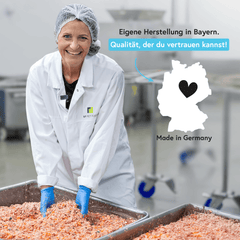 Lächelnde Frau im Labormantel bei der Fleischzubereitung in einer Produktionsumgebung.
