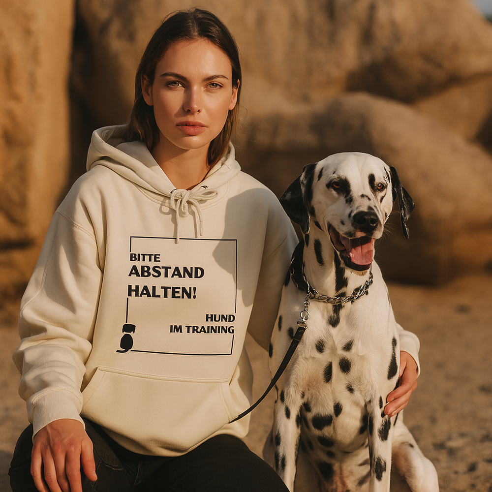 Hoodie Unisex "Abstand halten" in beige mit Aufdruck, junge Frau sitzt neben Dalmatiner in natürlicher Umgebung.