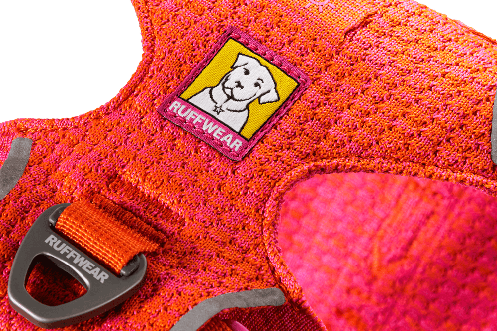 Hellrosa Ruff Wear Front Range® Flex Geschirr mit orangefarbigem Sicherheitsverschluss und gelbem Markenlabel für Hunde.