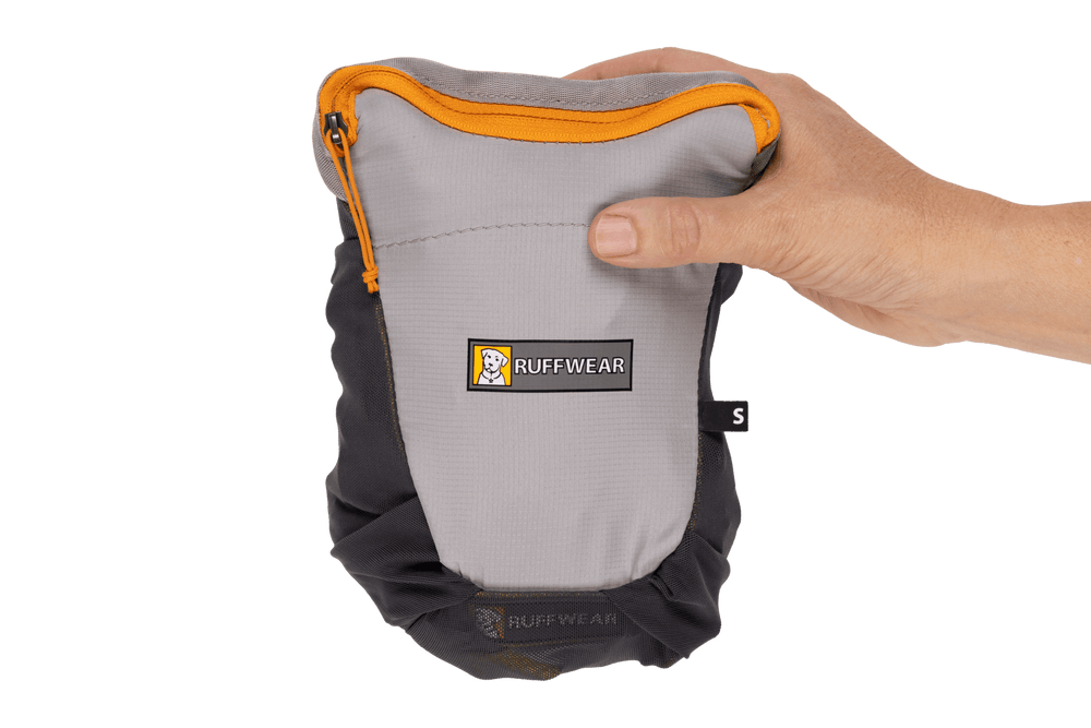 Hand hält kompakten grauen BackTrak™ Evakuierungsbeutel für Hunde mit orangefarbenen Akzenten und Reißverschluss.