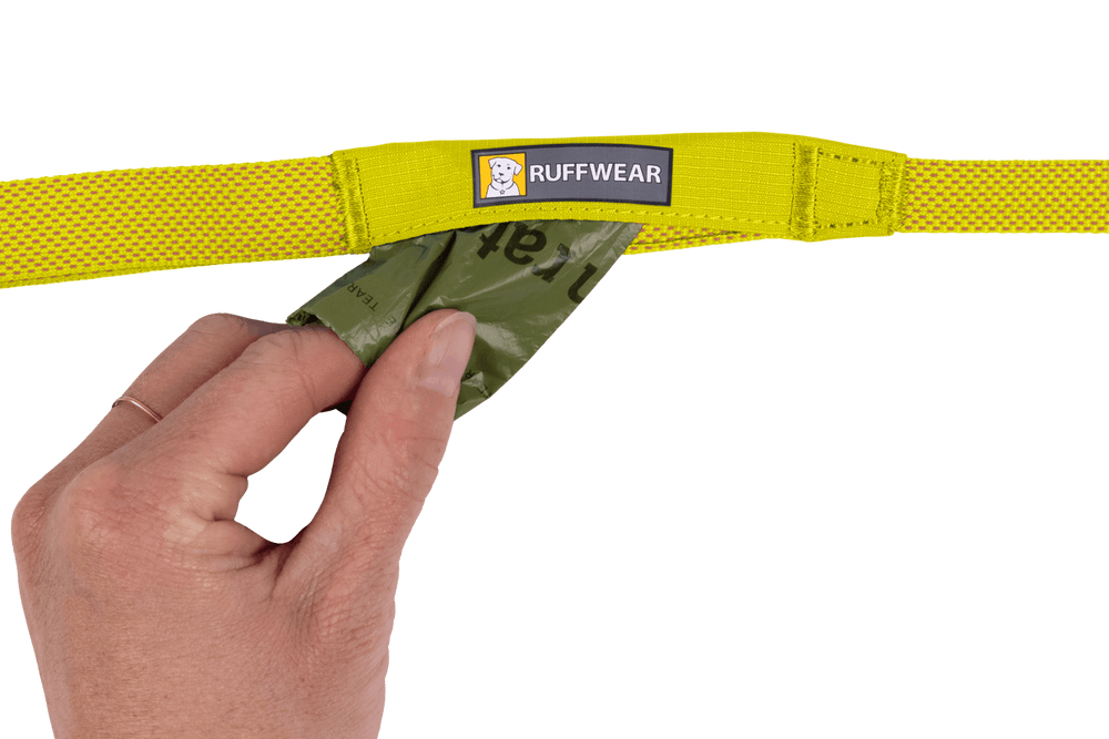 "Hand zieht grüne Tüte aus gelbem Hundehalsband mit Netzdesign von RUFFWEAR – Hi Light™ Hundeleine"