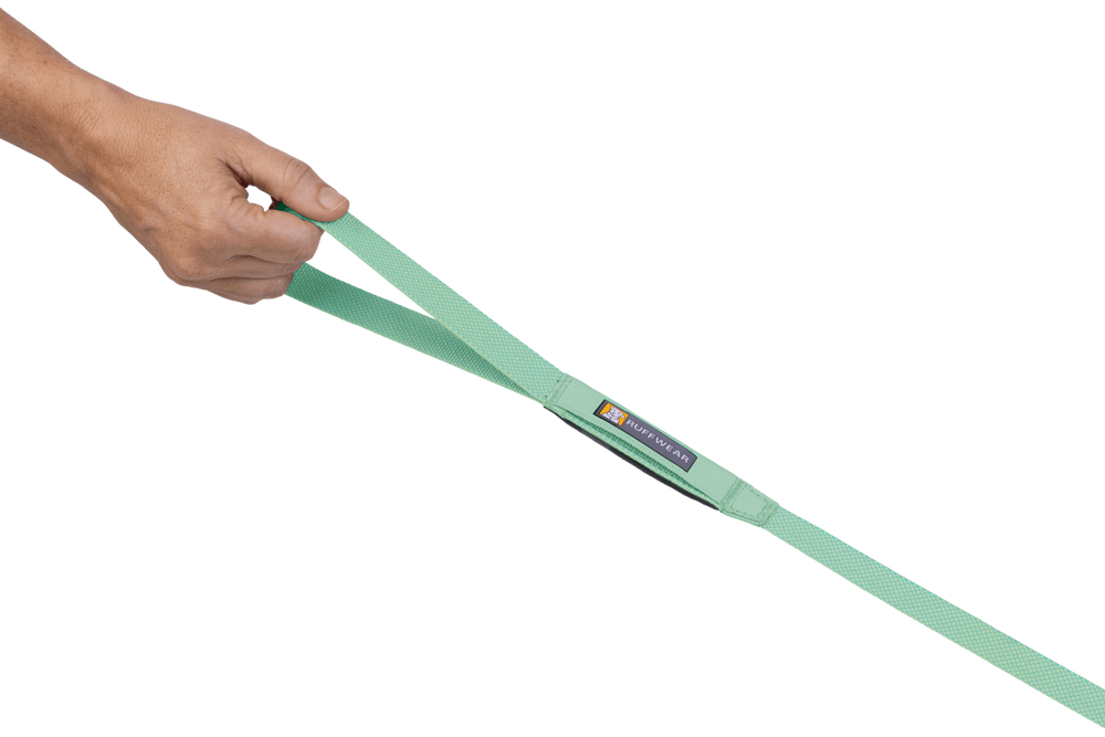Hand hält mintgrünen Hundeleinengriff aus gewebtem Material vor schwarzem Hintergrund.
