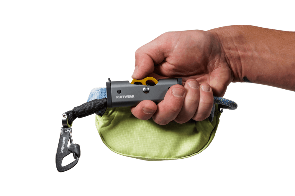 Hand mit grauem Griff und gelbem Knopf des Hitch Hiker™ Leinensystems, umgeben von einem hellgrünen Stoffmantel.