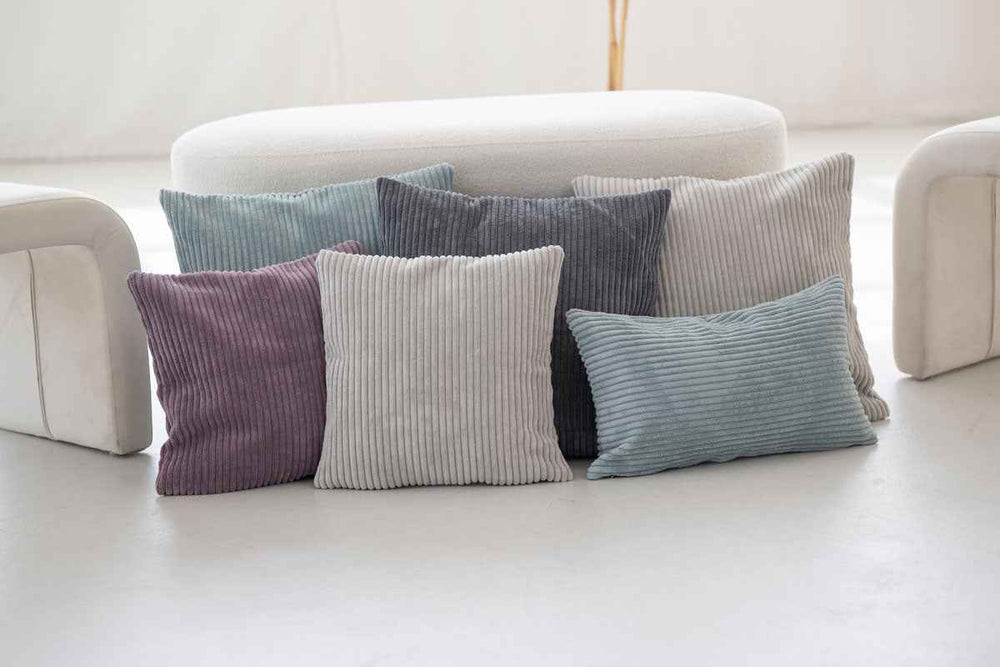 Bunte Kissenbezüge aus geripptem Cord in Blau, Grau, Lila und Beige auf einem hellen Untergrund.
