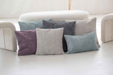 Bunte Kissenbezüge aus geripptem Cord in Blau, Grau, Lila und Beige auf einem hellen Untergrund.