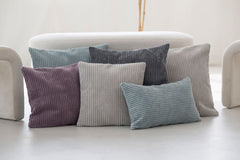 Bunte Kissenbezüge aus Cord in verschiedenen Farben und Texturen auf hellem Hintergrund angeordnet.