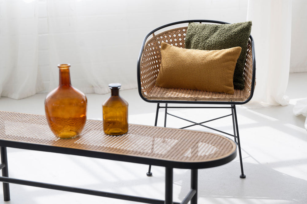 Moderner Stuhl mit schwarzem Metallgestell und Rattan-Sitzfläche, dekoriert mit olivgrünen und braunen Kissenbezügen.