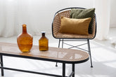 Moderner Stuhl mit schwarzem Metallgestell und Rattan-Sitzfläche, dekoriert mit olivgrünen und braunen Kissenbezügen.