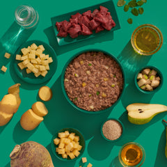 Hochwertiges FELIA Hirsch Nassfutter für Katzen, präsentiert mit frischen Zutaten auf grünem Hintergrund.