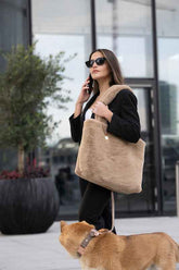 Modische Frau mit hellbrauner Handtasche, Sonnenbrille und Hund, umgeben von modernen Gebäuden und Pflanzen.