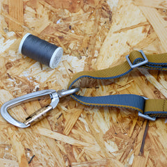 Silberner Kletterkarabiner mit Twist Lock auf Holzspanplatte neben grauem Faden und Kletterband.