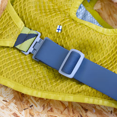 Gelbes meshähnliches Kleidungsstück mit blauem Gurt und Schnalle sowie finnischer Flagge im Hintergrund.