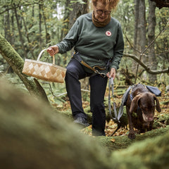 Person mit Gürteltasche Expedition Belt ECO wandert durch Wald mit Hund auf moosbewachsenem Pfad, grüner Pullover, dunkle Hose.