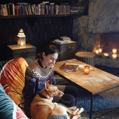 Person in gemütlichem Raum mit Hund, trägt Breezy Hygiene Pants ECO, vor Bücherregalen und Kamin mit Kerzen.