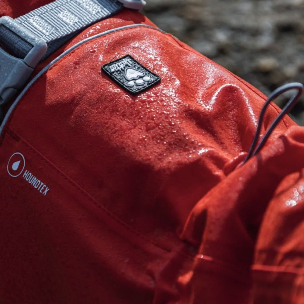 Roter, wasserabweisender Monsoon Coat mit Pfoten-Logo, wetterfest durch Houndtex, grauer und gelber Riemen sichtbar.