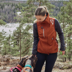 Frau mit orangefarbener Trainingsweste ECO interagiert mit Hunden im Wald.