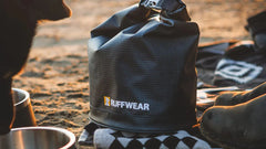 Faltbarer Kibble Kaddie™ Futtersack von Ruffwear auf sandigem Boden mit Zubehör für Haustiere.