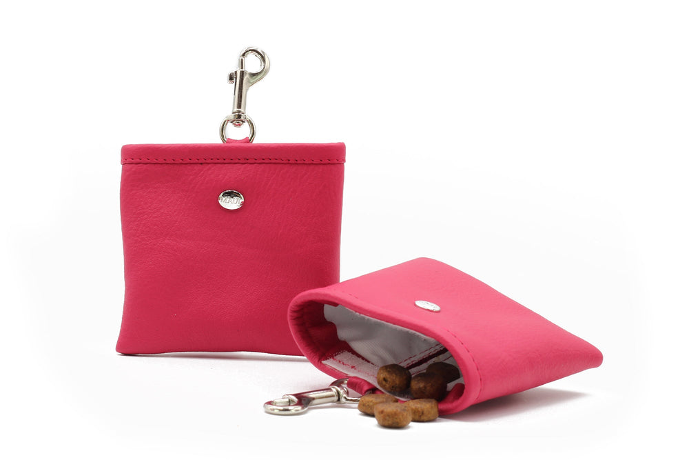 Pinke Leder-Geldbörse mit Druckknopfverschluss und Schlüsselanhänger, halb geöffnet und mit Leckerlis gefüllt.