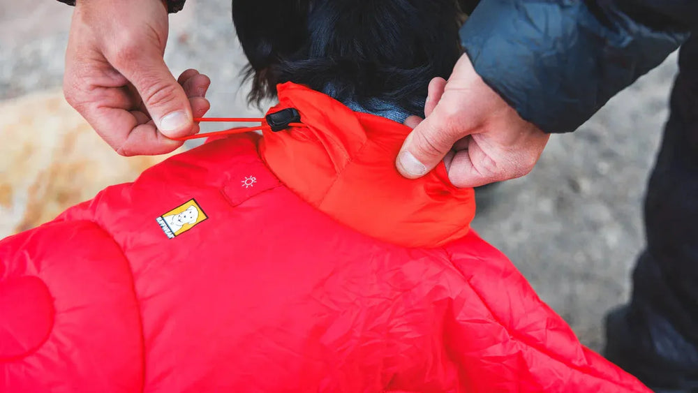 Person passt die Kapuze eines roten Palisades™ Schlafponchos in einer unscharfen, natürlichen Umgebung an.