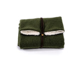 Grüne Reisedecke Forest, zusammengefaltet mit braunem Lederband, innen aus weißem, fellähnlichen Material.