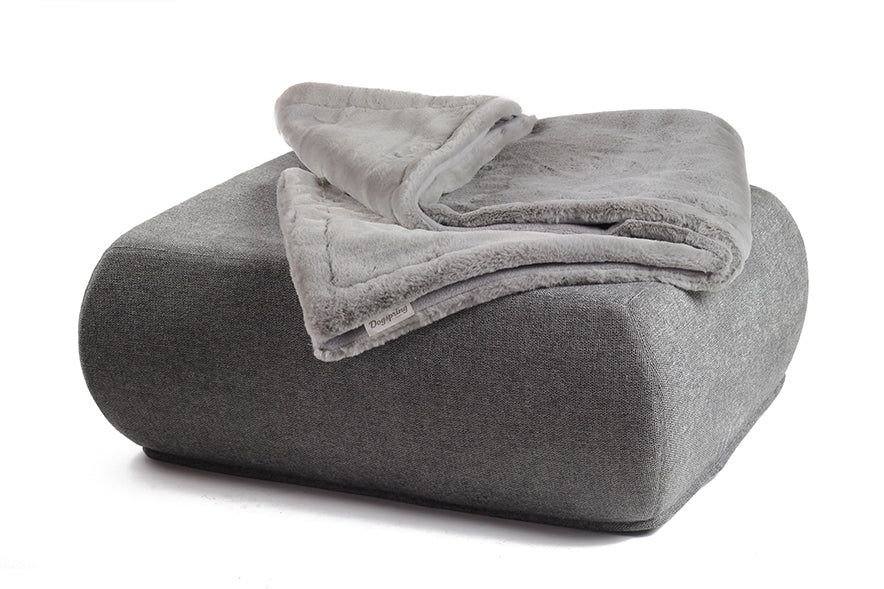Graue Wohndecke aus Webpelz auf einem quadratischen Pouf, auf weißem Hintergrund.