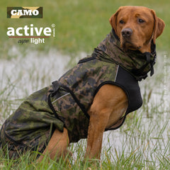 Hund in jagdlicher Outdoor-Weste im Camouflage-Muster, sitzt geschützt auf grünem Gras.